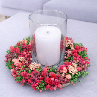 Celoročný sušený aranžmán so sviečkou v skle v ružovo-červených a zelených tónoch na bielom podnose, položený na konferenčnom stolíku v svetlej obývačke.