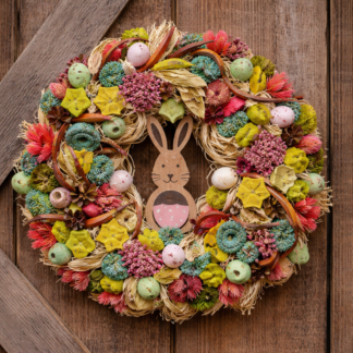 Veľkonočný veniec z rafie s farebnými sušenými kvetmi, dekoratívnymi vajíčkami a dreveným zajačikom na drevených dverách.