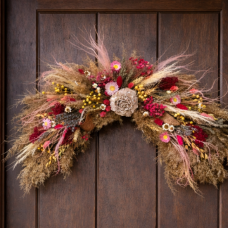 Netradičný veniec na dvere z obilnín, sušených tráv a červených kvetov umiestnený na drevených vchodových dverách