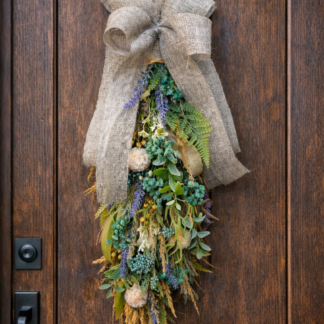 Prírodná dekorácia na dvere z eukalyptu, tráv a kvetov so jutovou mašľou zavesená na drevených vchodových dverách