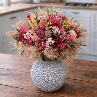 Sušená kytica v keramickej váze z prírodných tráv, obilnín a ružovo-červených sušených kvetov na drevenom stole v svetlej kuchyni