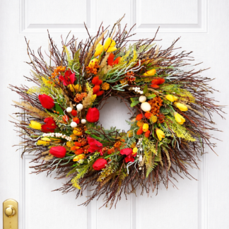 Farebný jarný veniec na dvere z prírodných konárikov s červenými a žltými tulipánmi, drobnými kvetmi a jarnou zeleňou na bielych vchodových dverách.