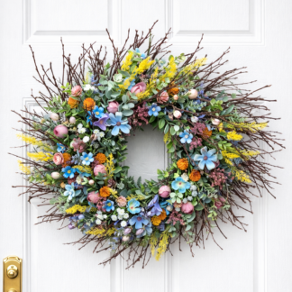 Veľký farebný jarný veniec na dvere z konárikov s modrými, ružovými a žltými kvetmi a eukalyptom na bielych vchodových dverách.
